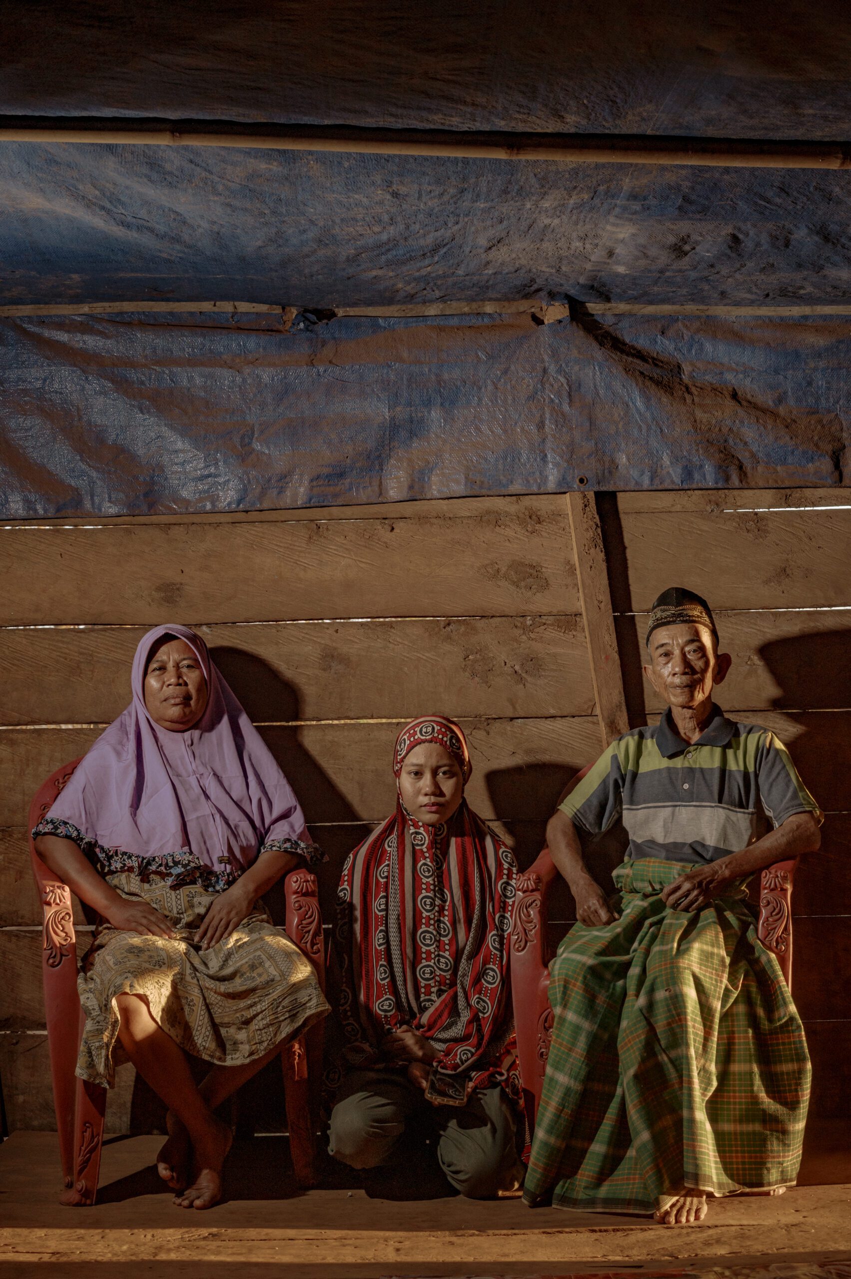 Yeni (kiri) , Sumiati (tengah) bersama Daeng Sanda (kanan) salah satu keluarga yang hidup berdampingan dengan smelter nickel milik PT Huadi Nickel-Alloy Indonesia,. Yeni, Daeng Sanda dan Sumiati cucunya adalah satu dari sekian banyak warga yang merasakan langsung dampak bising, polusi asap dan bau tak sedap saat pabrik pengelolaan nikel itu beroperasi karena hanya beberapa langka dari rumah kayu miliknya/Iqbal Lubis untuk Bollo.id