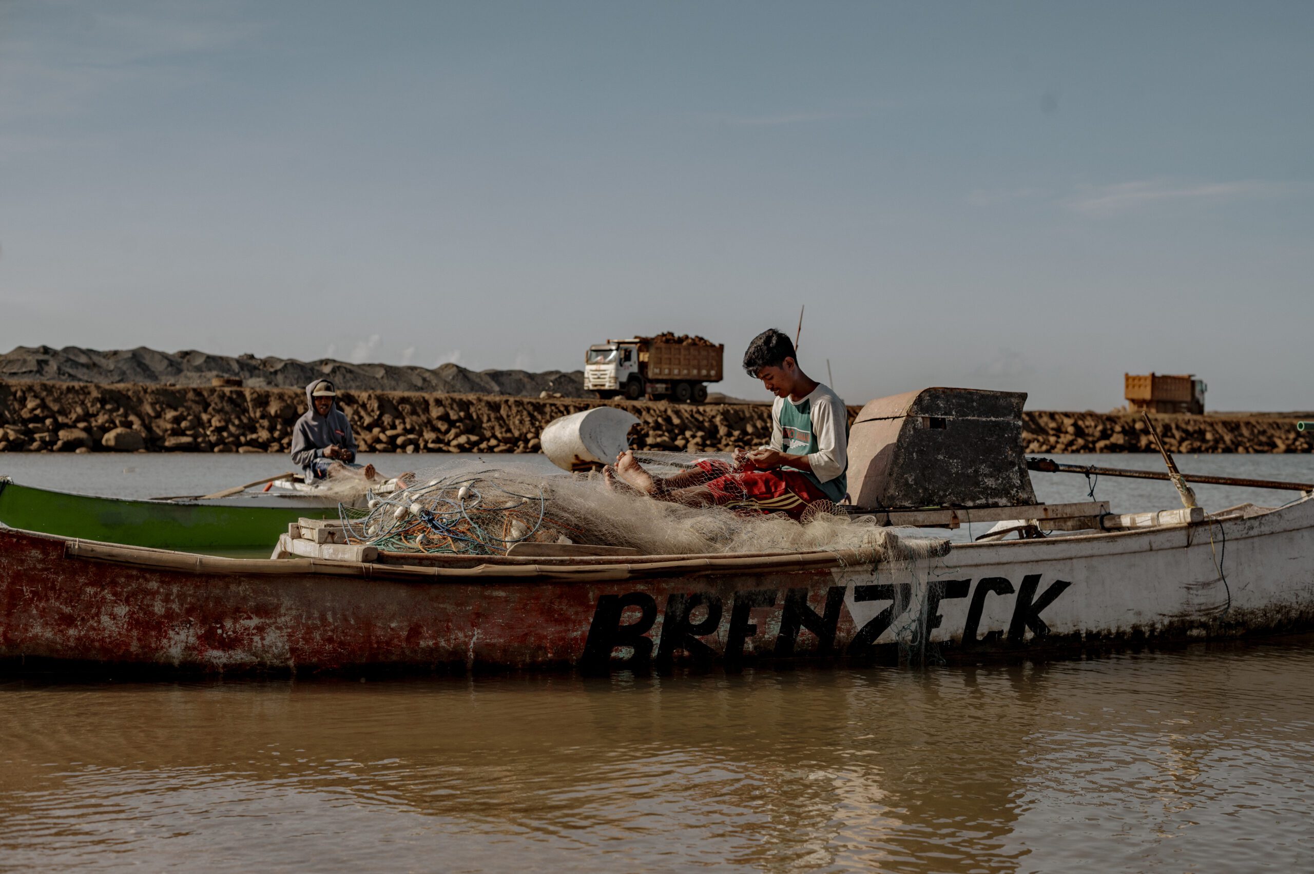 Nelayan menyiapkan jaring tangkapannya sembari beristirahat di pesisir dekat dengan dermaga Jetty milik PT Huadi Group. Air laut yang mulai terpapar limbah dan sisa bongkar muat nickel ore, Pihak paling terkena dampak akibat limpasan limbah adalah para petani rumput laut, yang jadi mata pencarian utama warga setempat. Tanaman rumput laut yang berada dekat dermaga jetty banyak yang rusak dan gagal panen/Iqbal Lubis untuk Bollo.id
