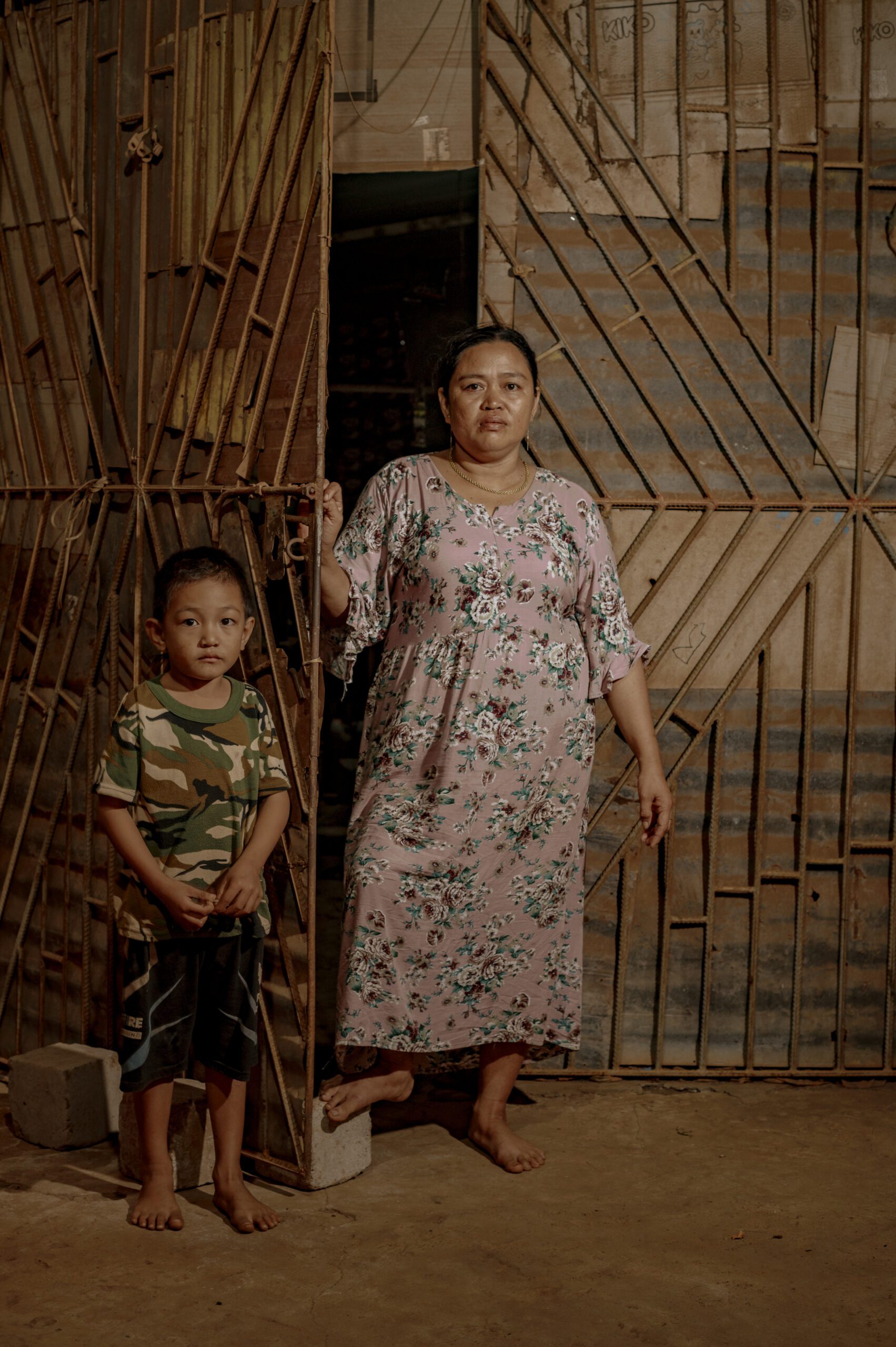 Risma, 41 tahun (kanan) bersama anaknya Cepang (kiri) berdiri di depan warung miliknya yang meski pun tetap berjualan tetapi pintu warung harus ditutup rapat-rapat agar debu tak masuk Di kampung Mawang, Desa Papan Loe/Iqbal Lubis untuk Bollo.id